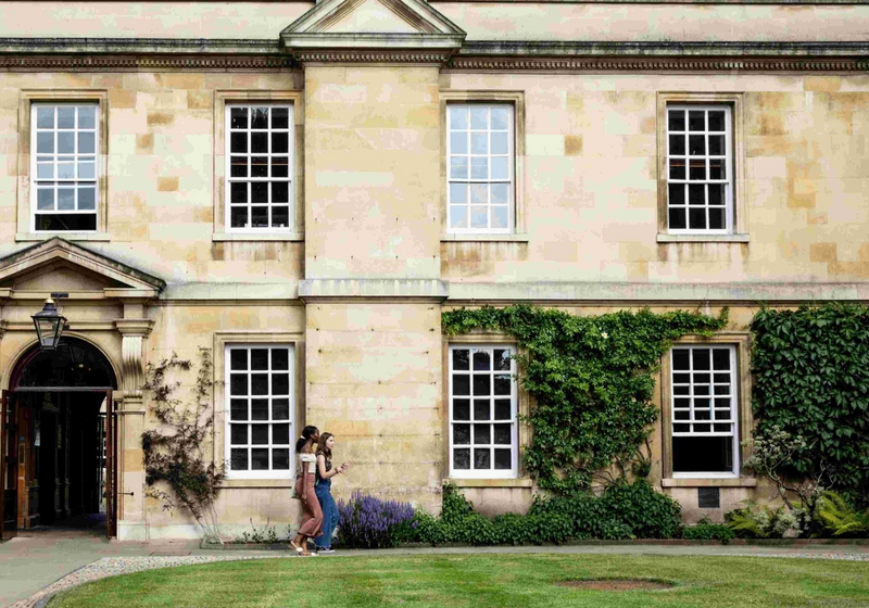 View of Trinity Hall College. Two Students walking past building in front of the lawn.