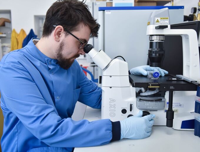 Student sitting, looking at sample through a microscope.